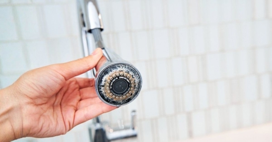 A woman is holding a chrome faucet covered with lime scale